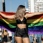 woman holding up gay pride flag at pride parade - clothes for pride featured image